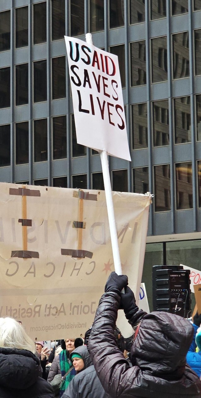 A protester in Chicago's Federal Plaza holds a sign that reads "USAID saves lives".