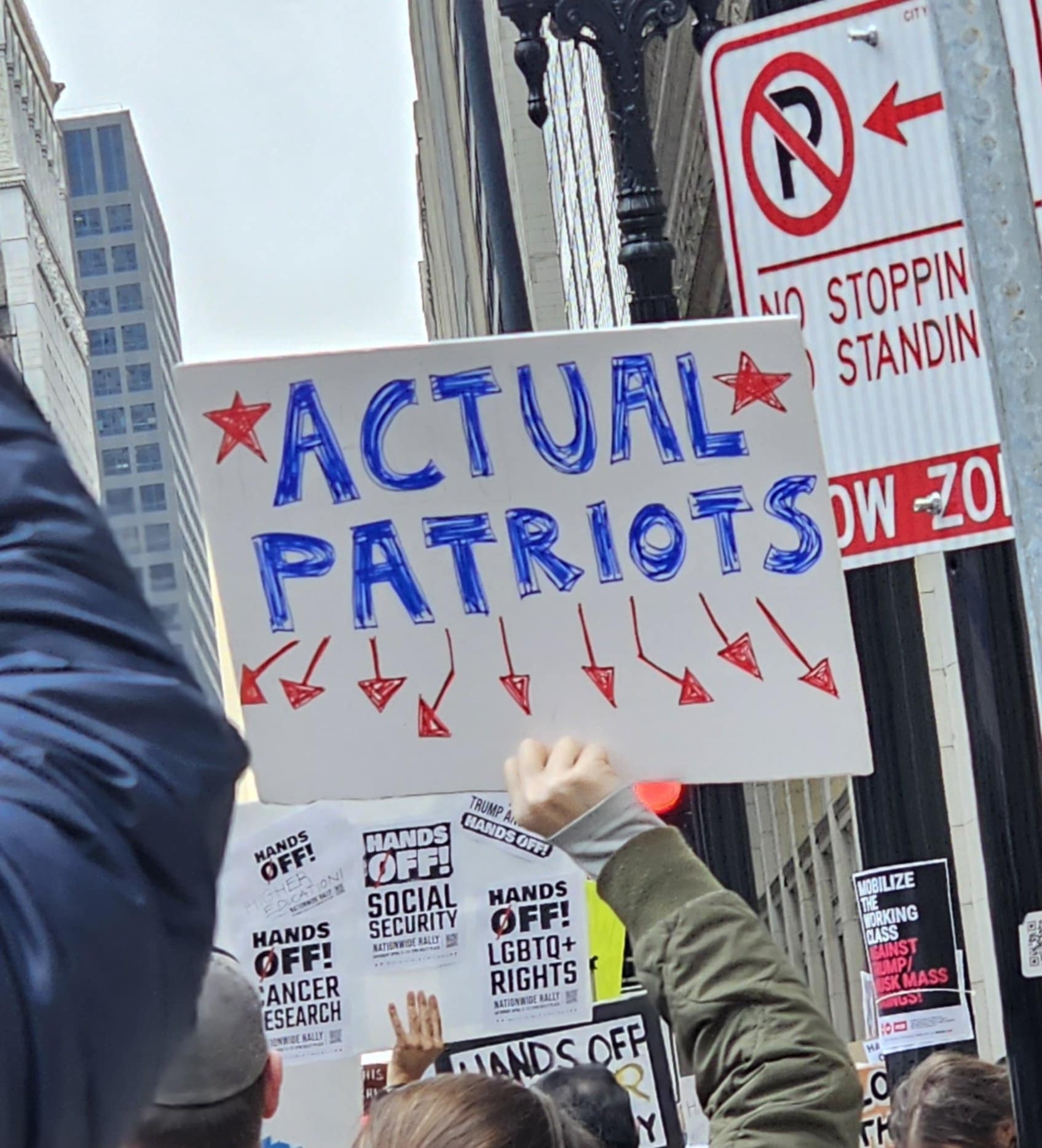 A protester holds up a sign that reads Actual Patrons with arrows pointing to the surrounding crowd on Chicago's LaSalle Stree.