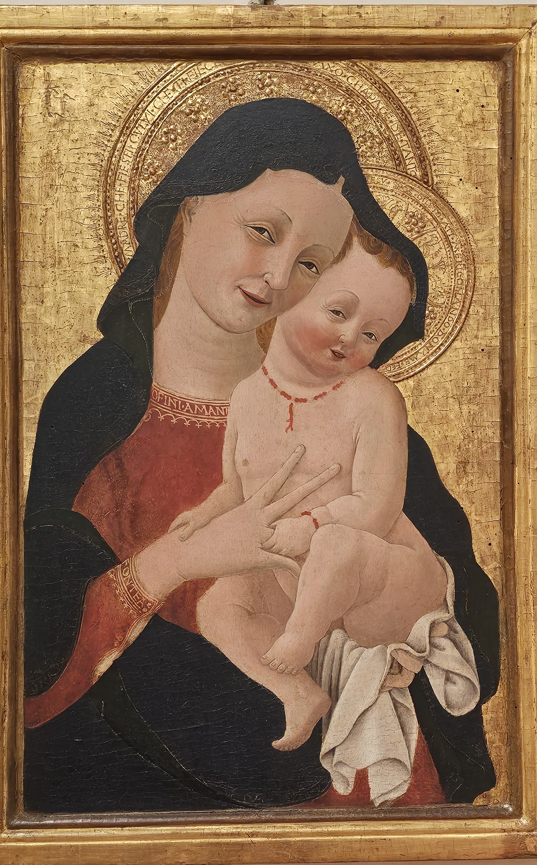 A sleepy-eyed Madonna with rosy cheeks that match that of her coy faced baby makes eye contact with the viewer with a half-smile.