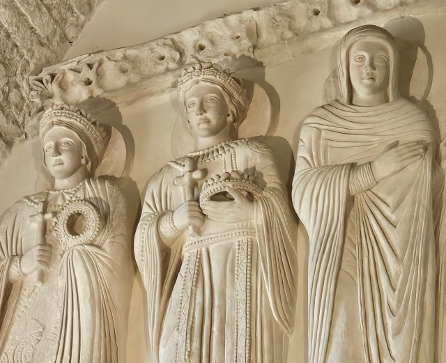 Three white sculptures of women with draped robes